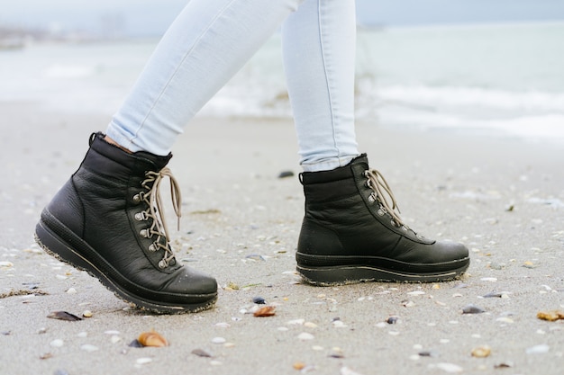 Vrouwelijke voeten in blauwe jeans en zwarte winterlaarzen liggen op het strandzand