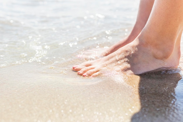 Vrouwelijke voeten in het zand bij de zee-surflijn