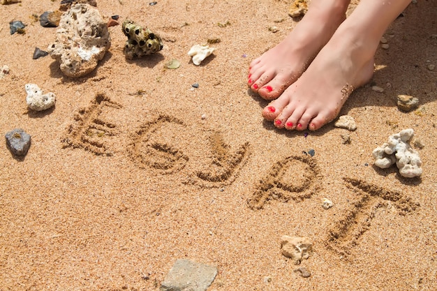 Vrouwelijke voeten met rode pedicure in strandzand met tekst Egypte