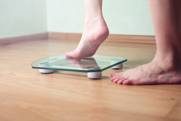 Vrouwelijke voeten staan op elektronische weegschalen voor gewichtsbeheersing