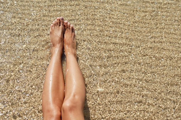 Vrouwelijke voeten tegen de zee op het strand van de zomer.