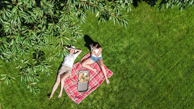 Foto vrouwelijke vrienden eten pizza op een zomerse picknick in het park ontspannen op het gras en hebben plezier met het uitzicht vanuit de lucht