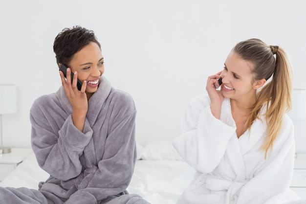 vrouwelijke vrienden in badjassen met behulp van telefoons op bed