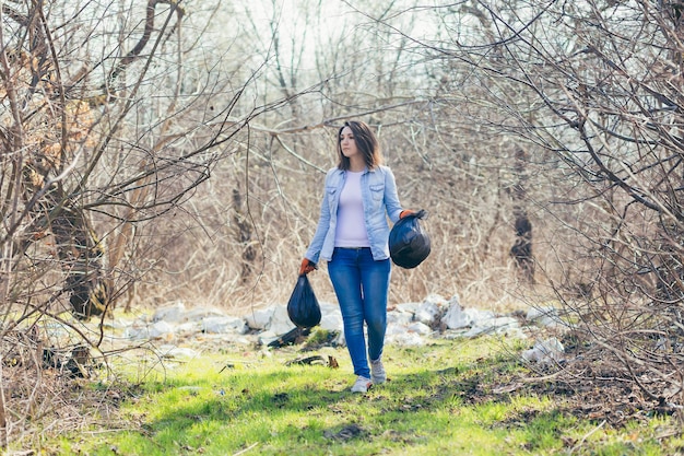 Vrouwelijke vrijwilliger houdt zakken met ingezameld plastic bij het schoonmaken van het bos en park van vuilnis