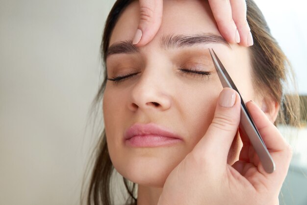 Vrouwelijke wenkbrauwen plukken met een pincet tijdens wenkbrauwcorrectie in de schoonheidssalon