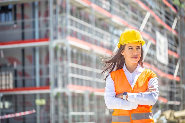 Vrouwelijke werfleider met veiligheidsvest en helm staat vol vertrouwen voor de constructie bedekt met steigers.