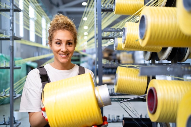 Foto vrouwelijke werknemer die draadspoel wisselt op een industriële breimachine in een textielfabriek