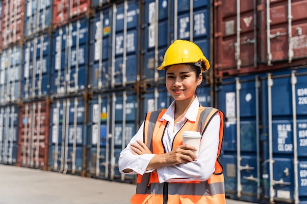 Vrouwelijke werknemer die staat en een gele helm draagt, controleert het laden en controleert de kwaliteit van containers van het vrachtvrachtschip voor import en export