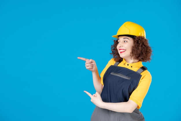 Vrouwelijke werknemer in geel uniform en helm op blauw