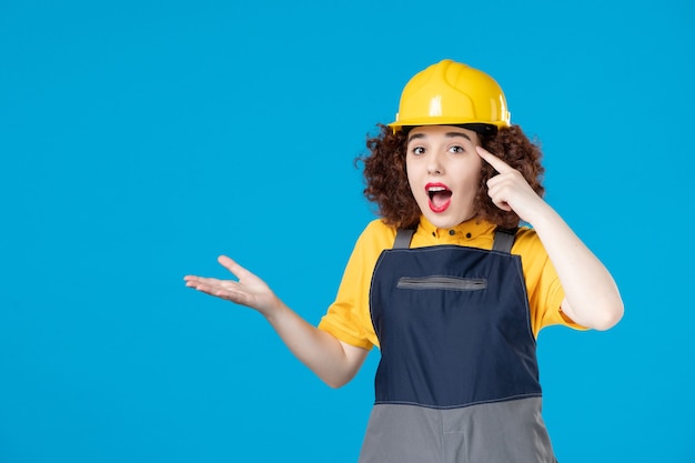 Vrouwelijke werknemer in geel uniform en helm op blauw