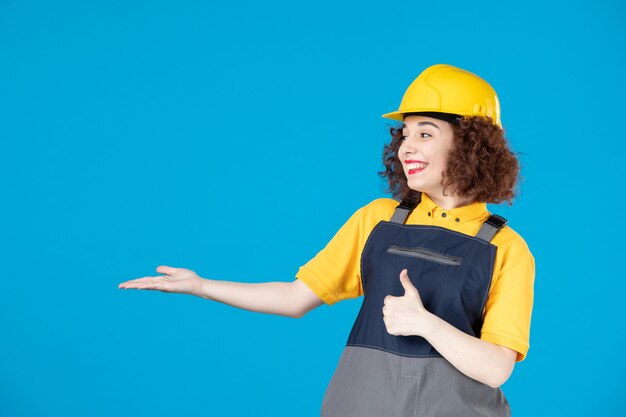 Vrouwelijke werknemer in geel uniform en helm op blauw