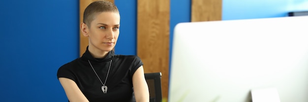 Vrouwelijke werknemer in stijlvolle kleding zit in een kantoor voor een computermonitor