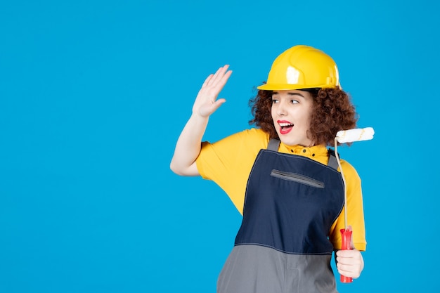 Vrouwelijke werknemer in uniform met verfroller op een blauw