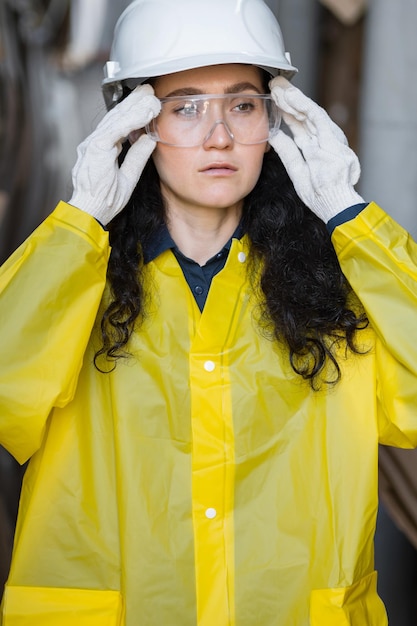 Foto vrouwelijke werknemer in witte veiligheidshelm die toezicht houdt op het proces in de afvalverwerkingsfabriek. controller met donker haar staat tegen stapels kartonnen afval