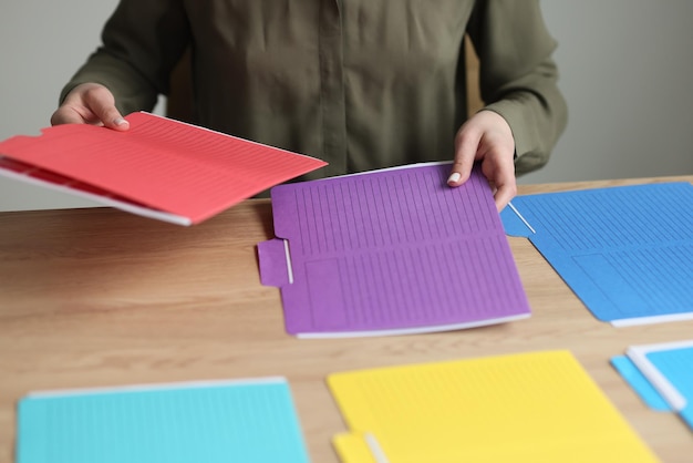 Vrouwelijke werknemer legt veelkleurige mappen met dossiers en documenten op houten tafel die vrouw neemt