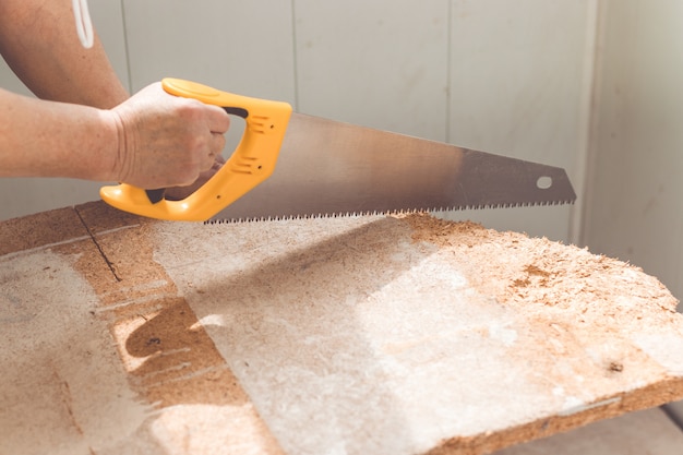 Vrouwelijke werknemerhanden die een houten raad in een workshop zagen