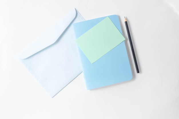 Vrouwelijke werkruimte met blanco open notitieboekje voor schrijven, pen en envelop voor brieven op een witte tafel. Bovenaanzicht, plat lag, kopieer ruimte, minimalisme.