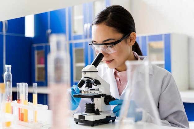 Vrouwelijke wetenschapper in het laboratorium dat door microscoop kijkt