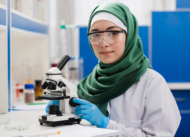 Vrouwelijke wetenschapper met hijab die in laboratorium met microscoop werkt