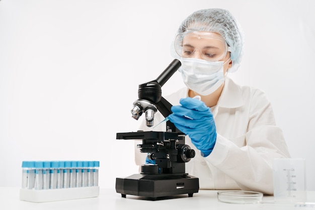 Vrouwelijke wetenschapper werkt met krachtige microscoop en speciaal reagens om coronavirus-test te maken