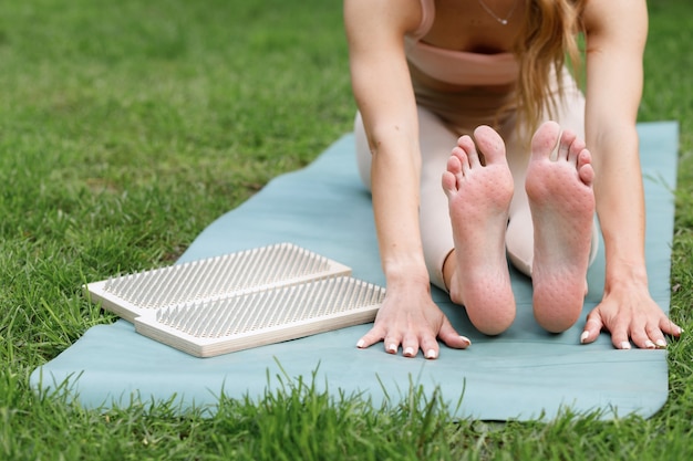 Vrouwelijke yogavoeten met deuken van een plank met spijkers op een groen gazon. yoga training