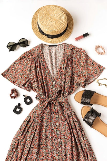 Vrouwelijke zomer esthetische mode kleding samenstelling met sundress pantoffels zonnebril stro hoed oorbellen op witte achtergrond plat lag bovenaanzicht minimale doek concept