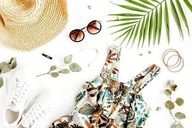 Vrouwelijke zomer street style zomerjurk strohoed sneakers zonnebril en tropisch blad bovenaanzicht fl