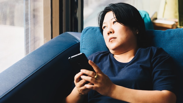 Vrouwen 40s die van Azië smartphone houden die op bank denken