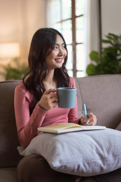 Vrouwen die naar buiten kijken, genieten dromerig terwijl ze thee drinken en een dagboek schrijven in hun levensstijl thuis