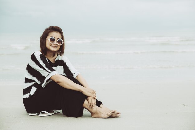 Vrouwen die van portret de Aziatische enige hipsterindy eenzame zonnebril dragen situerend alleen op het strand