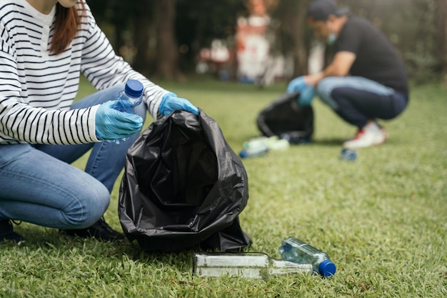 Vrouwen en mannen bewaren plastic afvalflessen in zwarte zakken in het park in het ochtendlicht