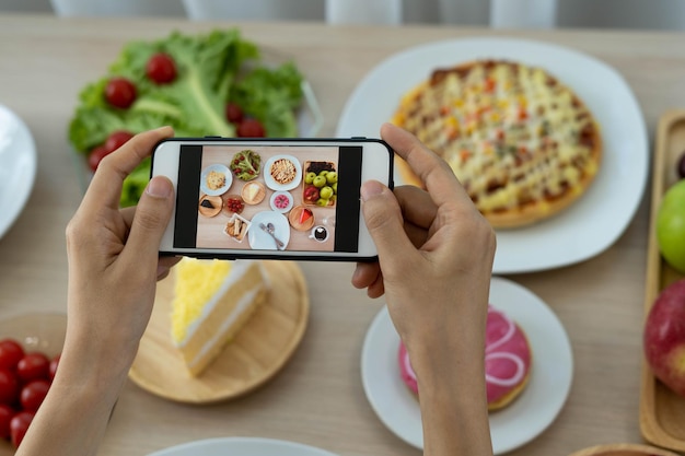 Vrouwen gebruiken mobiele telefoons om foto's van eten te maken of om live video's te maken op sociale netwerktoepassingen Eten voor het diner ziet er smakelijk uit Fotografie en foto's maken voor beoordeling voedselconcepten