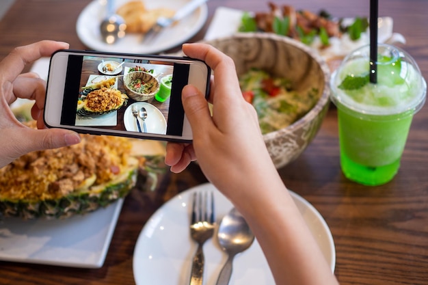 Foto vrouwen gebruiken mobiele telefoons om foto's van eten te maken of om live video te maken op sociale netwerktoepassingen. eten voor het avondeten ziet er smakelijk uit. fotografie en foto maken voor beoordeling van voedselconcepten