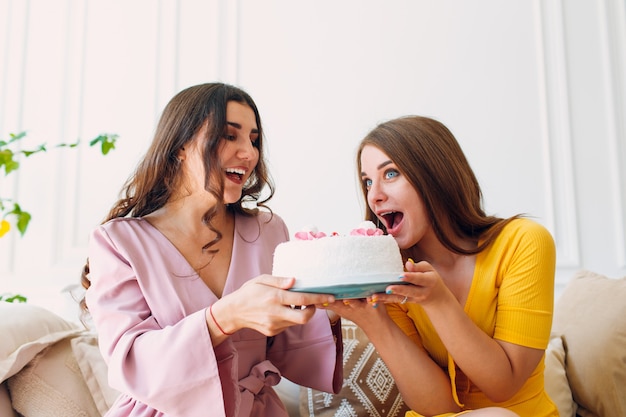 Vrouwen gelukkige vrienden thuis zitten en eten witte verjaardagstaart.