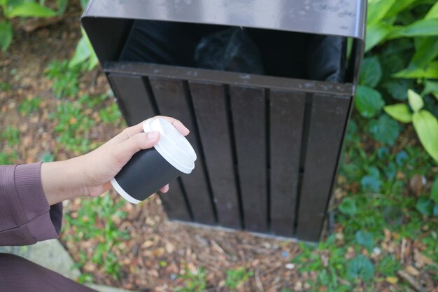 Vrouwen gooien met de hand een lege koffiekopje in de vuilnisbak of vuilnisbak