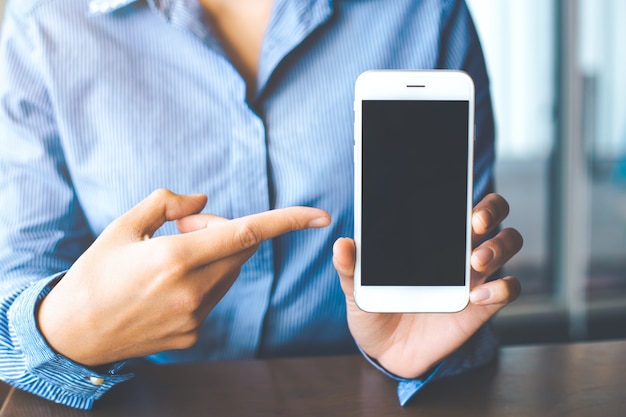 Vrouwen hand tonen de witte mobiele telefoon op het lege scherm op kantoor.