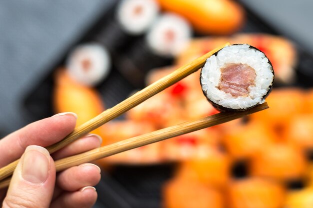 Vrouwen handen houden sushi rol met stokken close-up vervaagde donkere achtergrond