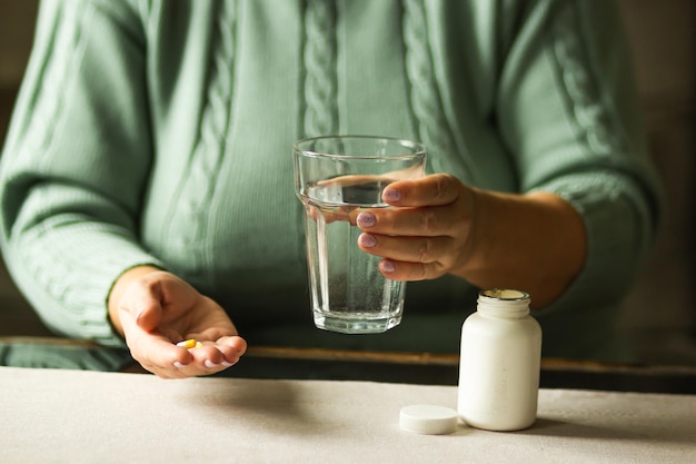 Vrouwen handen houdt twee capsules en een glas water over de tafel klaar om medicijnen te nemen