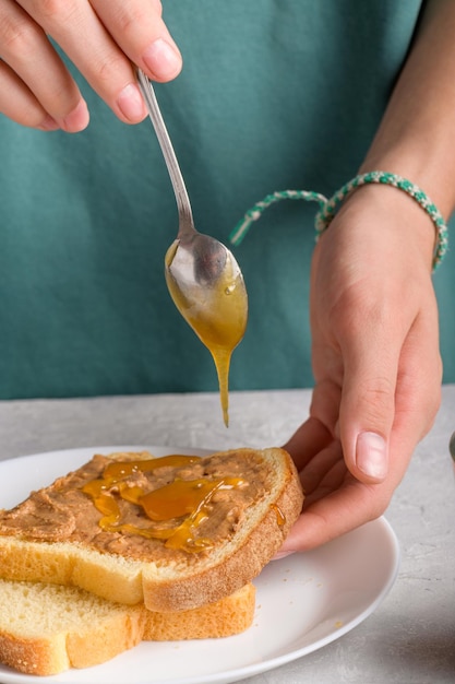 Vrouwen handen zetten honing met lepel op een toast met pindakaas om een boterham te maken voor het ontbijt