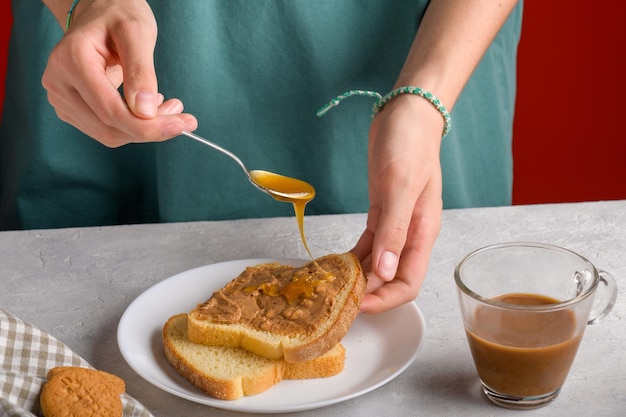 Vrouwen handen zetten honing met lepel op een toast met pindakaas om een boterham te maken voor het ontbijt