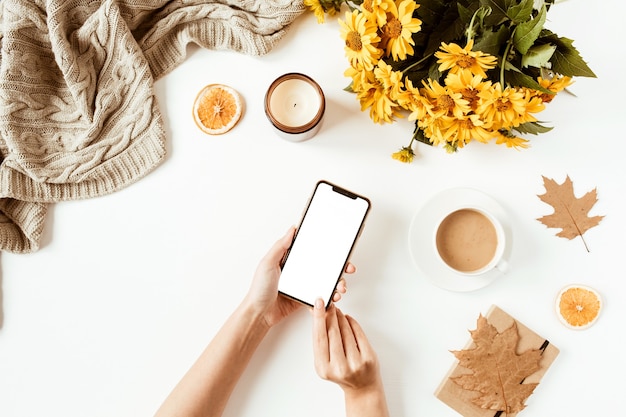 Vrouwen houden mobiele telefoon in de hand. Thuiskantoor tafel bureau werkruimte. Plat lag, bovenaanzicht meisje baas bedrijfsconcept. Deken, bloemenboeket, bladeren, koffiekopje