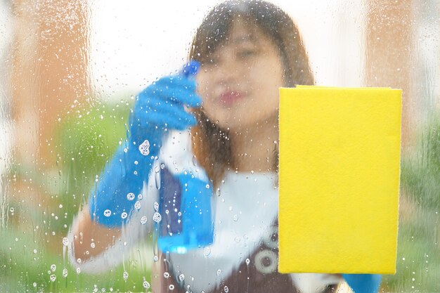 Vrouwen huishoudster die de spiegel met gele spons schoonmaken