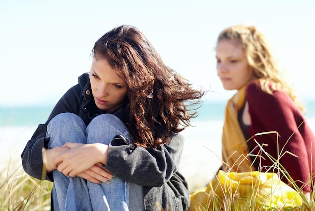 Foto vrouwen in de geestelijke gezondheidszorg zitten apart na een meningsverschil en op een veld buiten gefrustreerde of verdrietige angst of depressie en familiezusters die samen buiten in de natuur overstuur of depressief zijn voor slecht nieuws