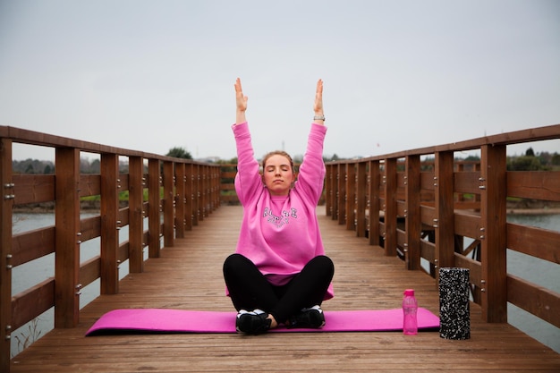 Foto vrouwen in roze hoodie die in de herfst buiten op de pier oefeningen doen