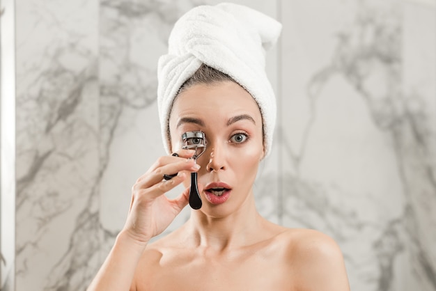 Vrouwen krullende wimpers met krulspeld in badkamers na douche