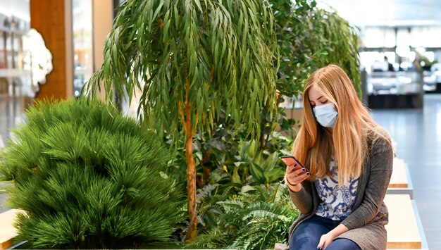 vrouwen met maskers Zitten in winkelcentrum, met telefoon, sociaal verspreid.