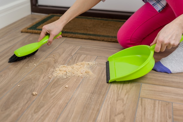 Vrouwen schoonmakende vloer met bezem en stofpan