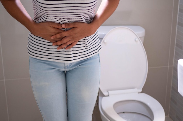 Vrouwen staan voor de deur van de badkamer en gebruiken hun handen om de buik vast te houden met hevige buikpijn of diarree Het concept van maagkrampen diarree