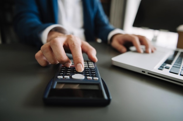 Vrouwen tellen munten op rekenmachine en nemen van de spaarpot hand met pen die aan rekenmachine werkt om op bureau te berekenen over kosten thuiskantoorxAxA