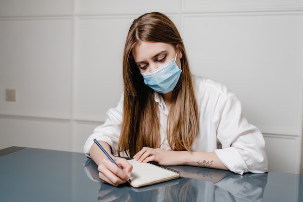 Vrouwen thuis bureau die masker dragen en nota's in notitieboekje schrijven